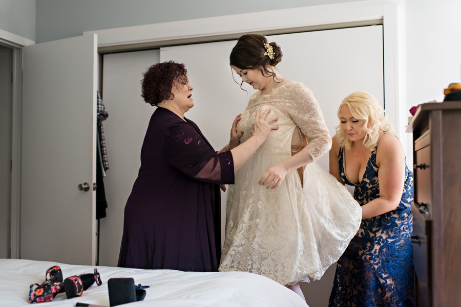 The brides mother helps her daughter put on her wedding dress.